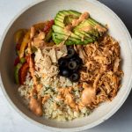 shredded chicken and cauliflower rice and peppers in a bowl topped with chipotle sauce