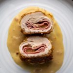 Chicken Cordon Bleu on a white plate with some creamy mustard sauce