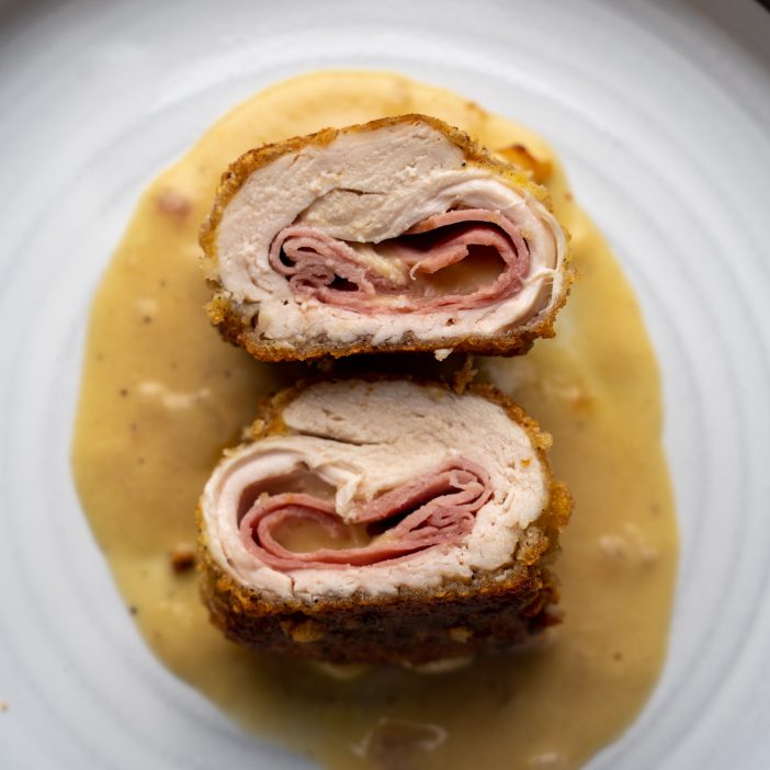 Chicken Cordon Bleu on a white plate with some creamy mustard sauce