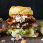 Beef slider topped with fried cheese, guacamole, pic de Gallo, southwest ranch, on a bun.